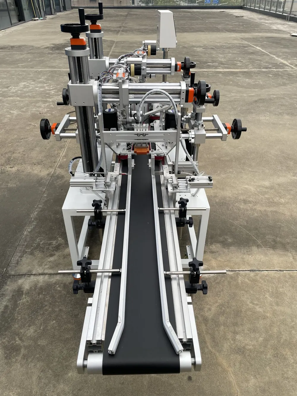 Clamping-Belt Dual-Head Tape Applicator — View along the conveyor with its side guides