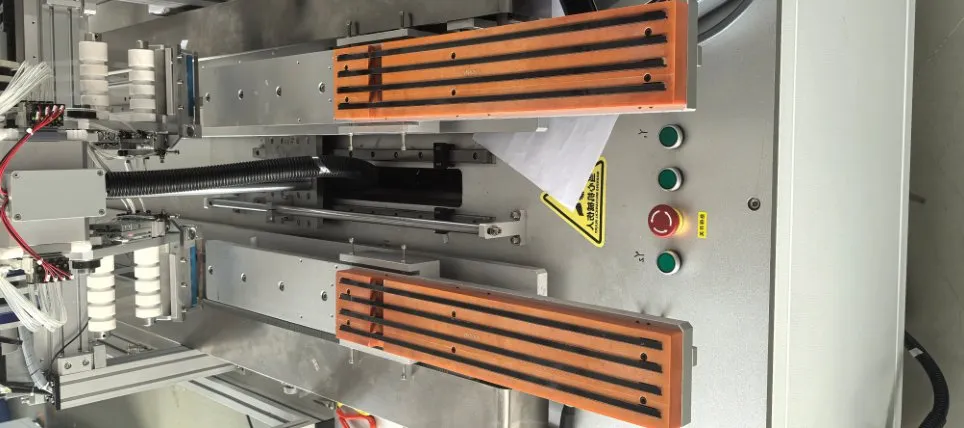 Dual-Head Tape Applicator with Magnetic Unloading — Parts on the fixtures with several tape strips applied at once (inside the machine)